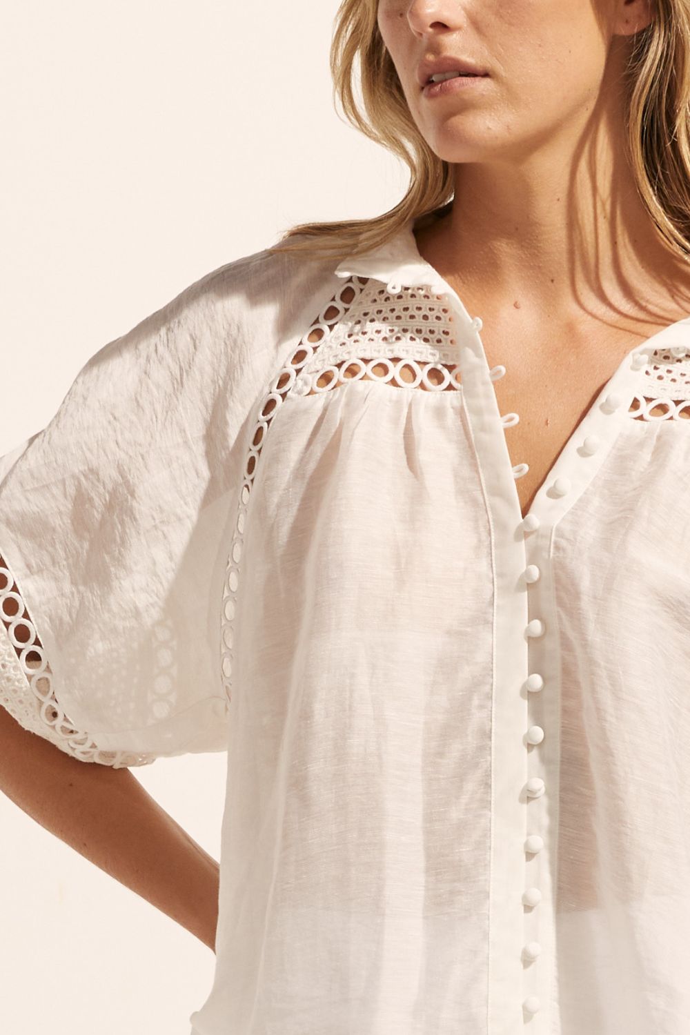 white, top, high neck, mid-length sleeve, covered buttons, circular lace detailing, close up image